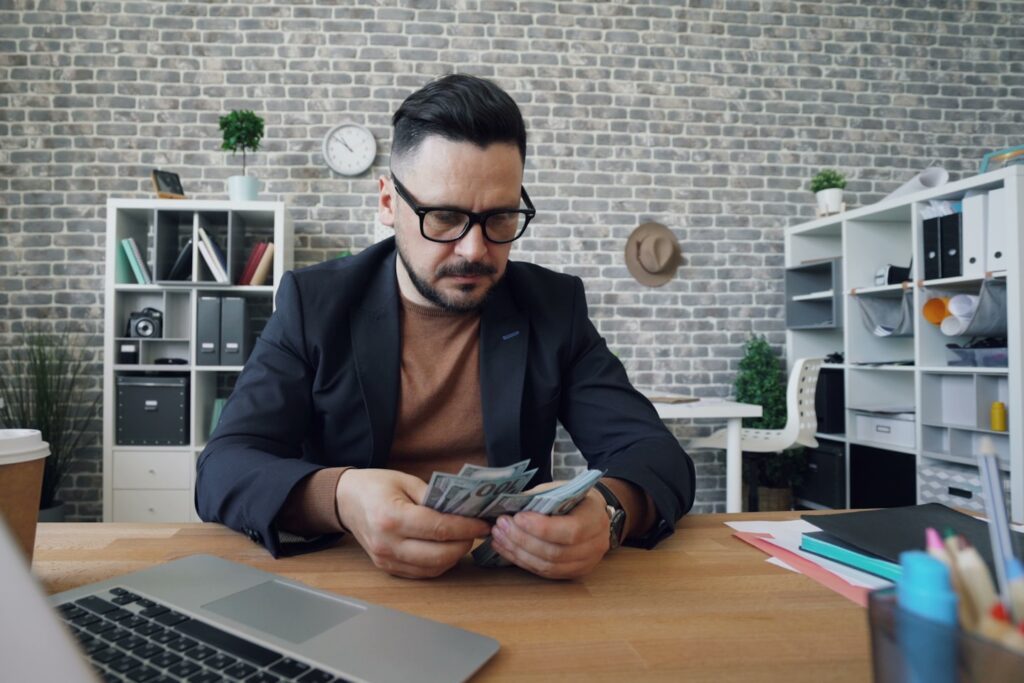 Serious businessman counting money dollars sitting at desk in office alone
